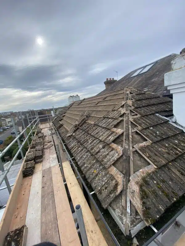 Weathered concrete tiles being stripped from a hipped roof from scaffolding